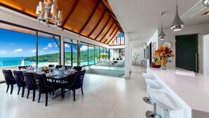 Un espace repas moderne avec vue sur l’océan, une cuisine dotée d’un plan de travail blanc et une table à manger dressée pour six personnes.
