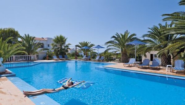 A swimming pool with lounge chairs and umbrellas, surrounded by palm trees and a building. - Tersanas Village Apartments (Chania)
