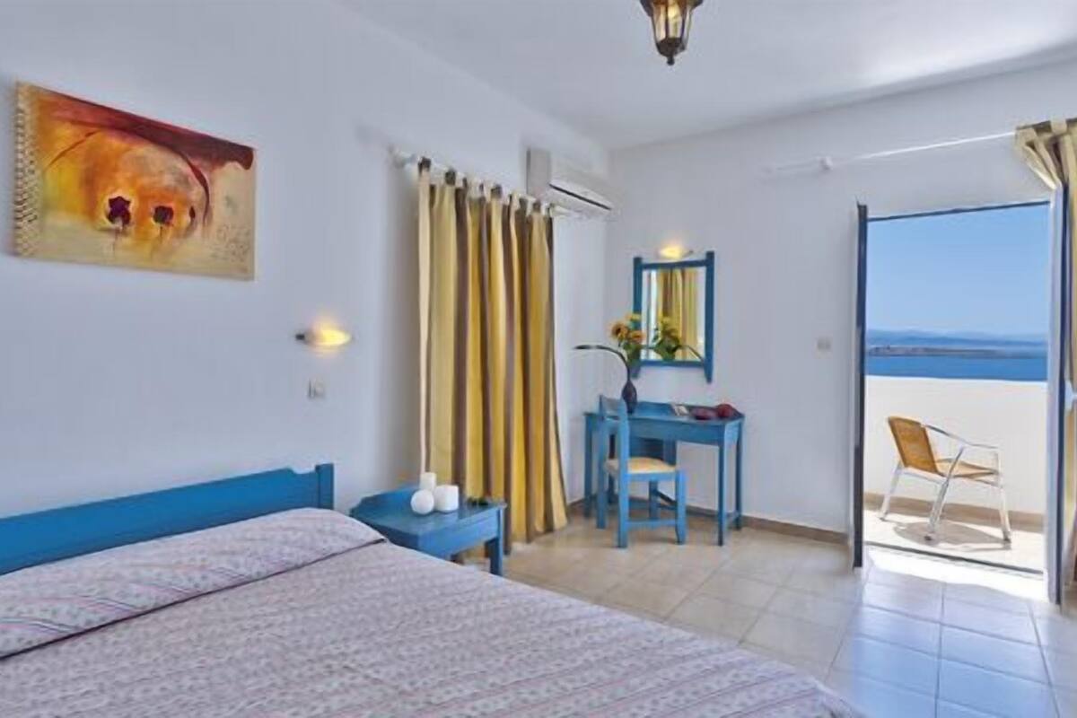 A hotel room with a bed, a desk, a chair, and a view of the sea through a balcony.