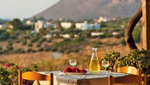 A table set outdoors with a bottle of yellow liquid, a glass, and a plate of red grapes. - Tersanas Village Apartments (Chania)