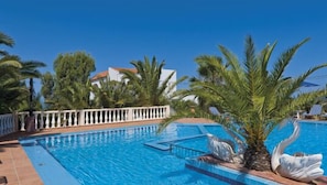 A swimming pool with a white balustrade, palm trees, and a building in the background.