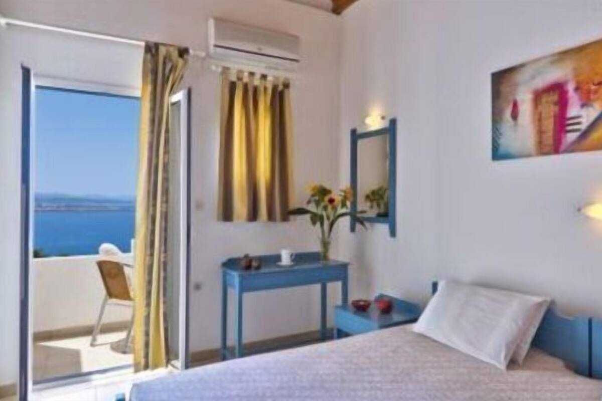A hotel room with a bed, a desk, a chair, and a view of the sea.