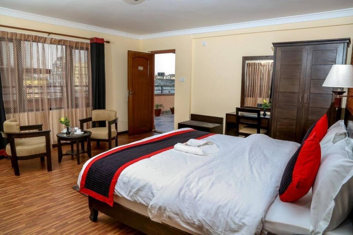 A hotel room with a bed, a desk, a chair, a wardrobe, and a view through a window.