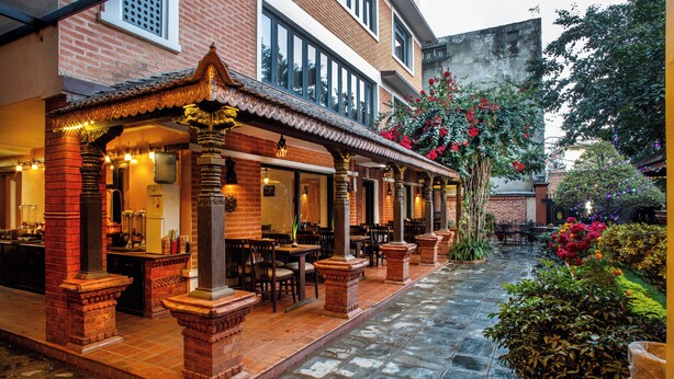 Un restaurante con terraza, columnas de ladrillo y un patio con baldosas.