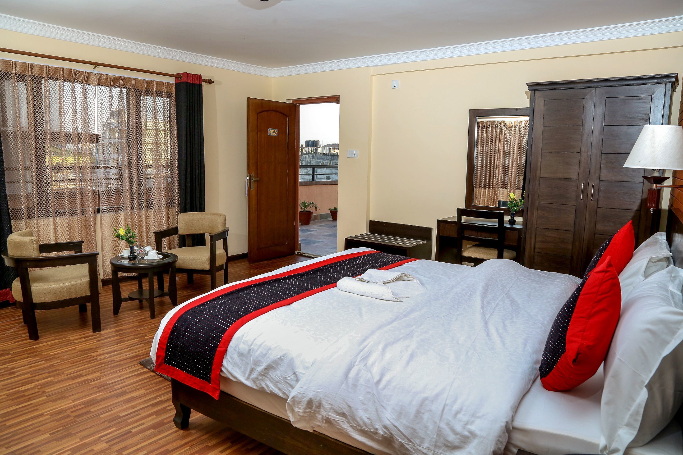 A hotel room with a bed, a desk, a chair, a wardrobe, and a view of the outside.