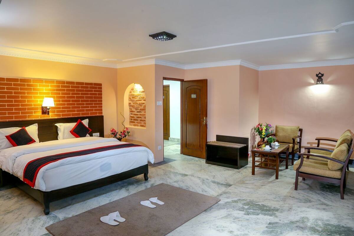 A hotel room with a bed, a desk, a chair, a door, and a wall-mounted light fixture.