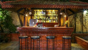Un bar con mostrador de ladrillo, tres taburetes y un cantinero.