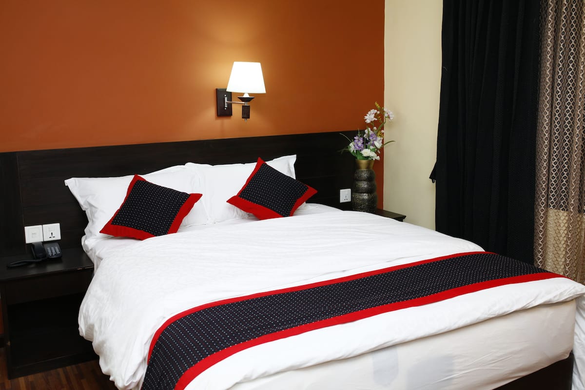A hotel room with a large bed, a nightstand with a phone, a lamp, and a vase with flowers.