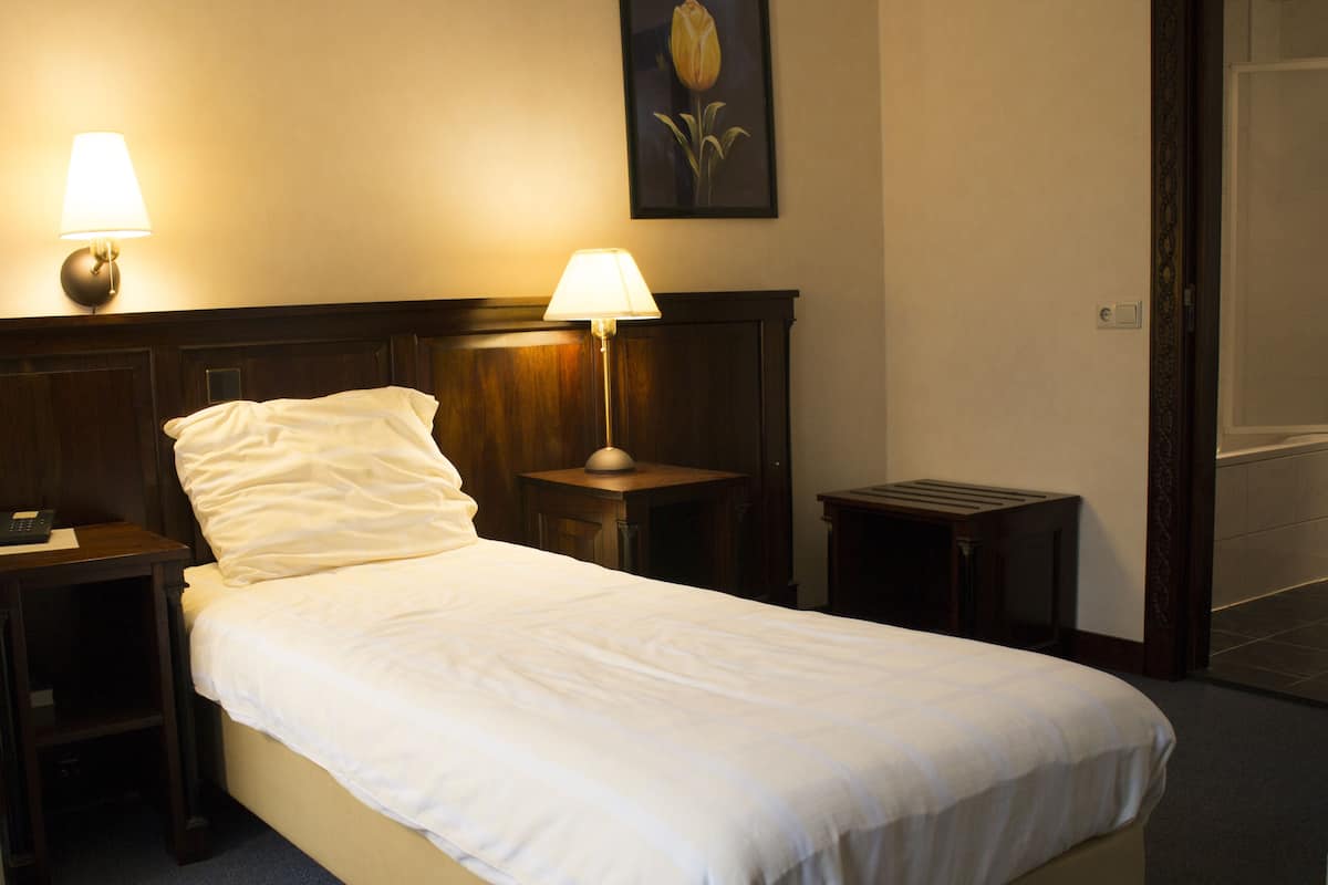 A neatly made bed with white linens, two bedside lamps, a small wooden nightstand, and a framed picture on the wall.