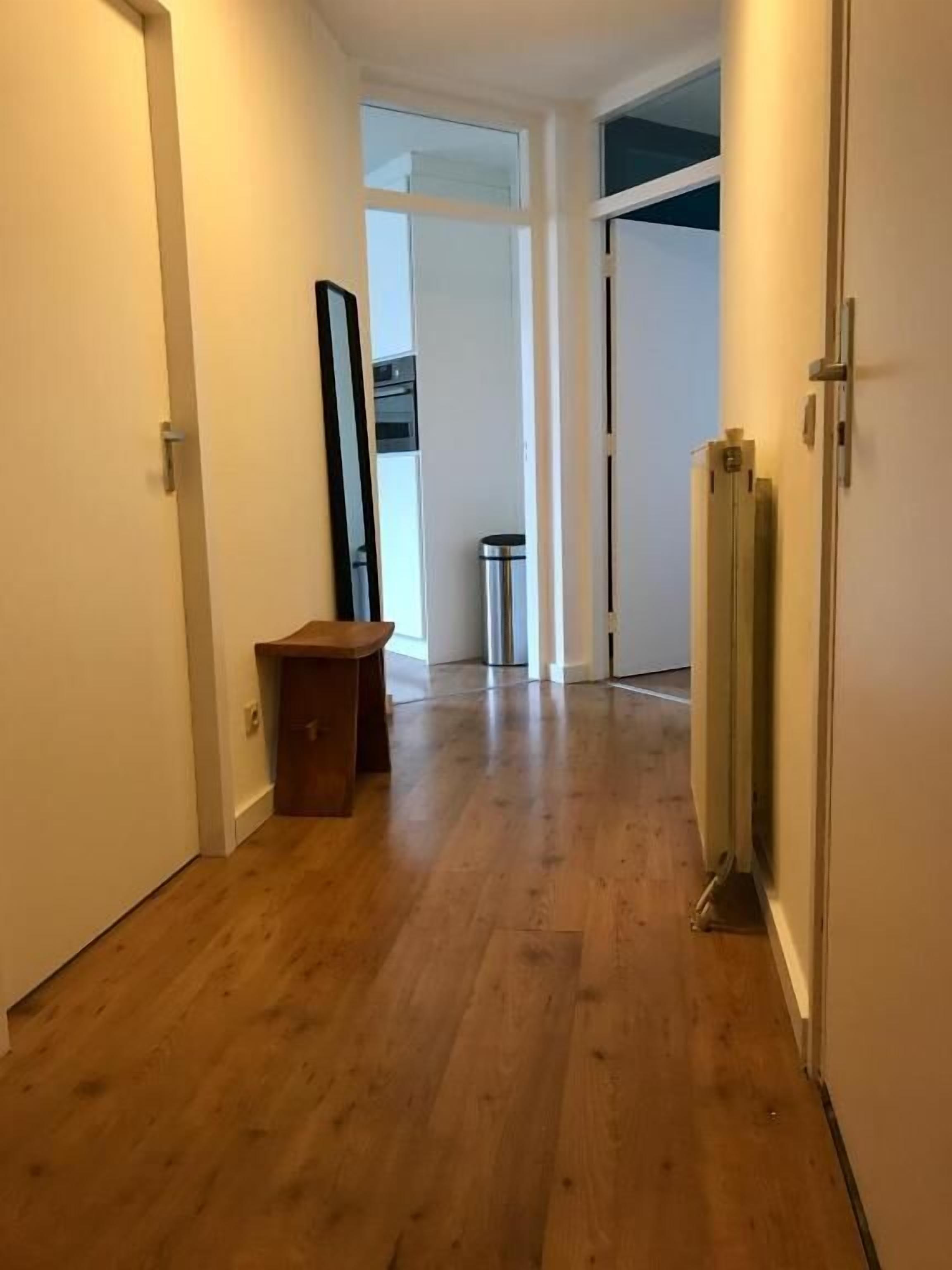 A hallway with wooden flooring, a door on the left, and a radiator on the right.