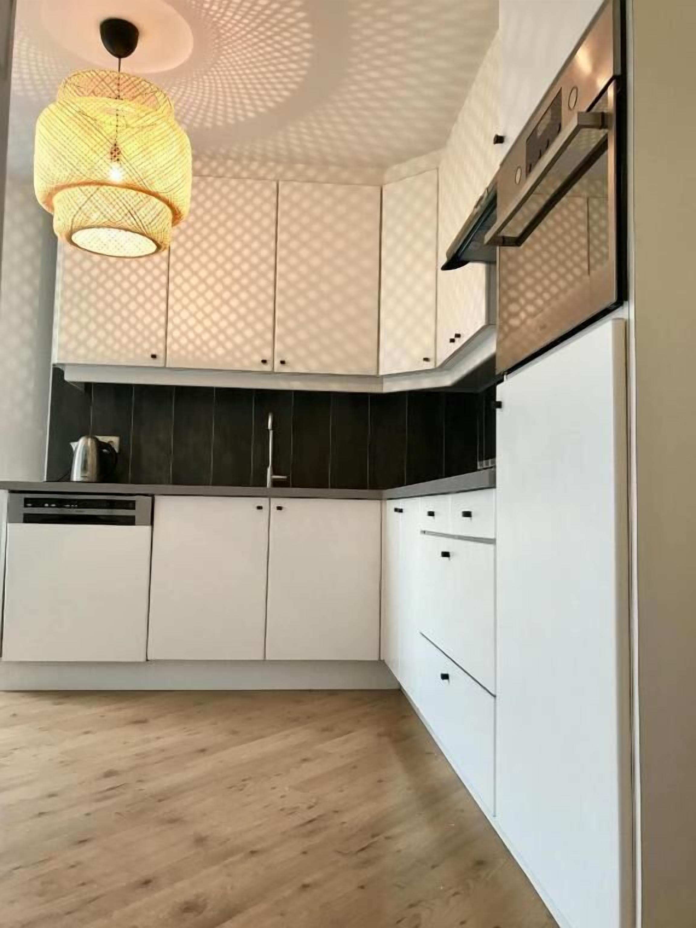 Una cocina con gabinetes blancos, encimera negra y una lámpara colgante.