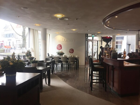 Interior de un restaurante con mesas y sillas, una zona de bar y una pared con el logotipo 'de LOBBY'.