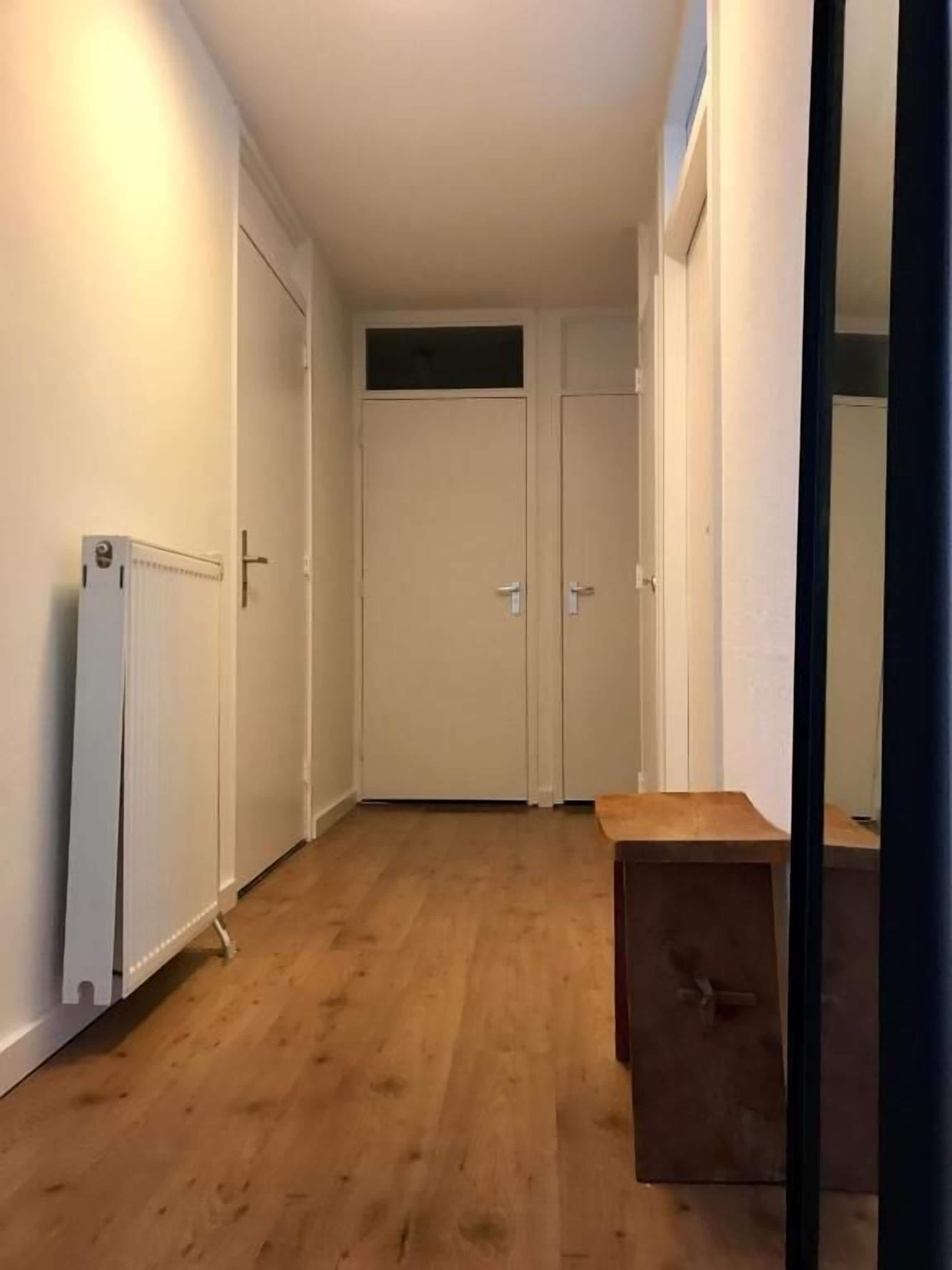 A narrow hallway with wooden flooring, a radiator, and a wooden cabinet.