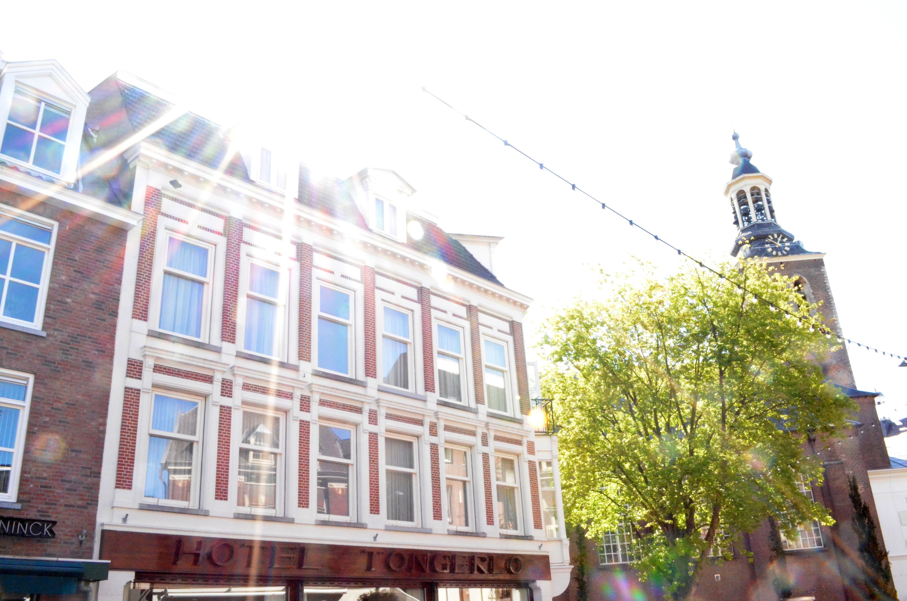 A hotel with a traditional facade, a visible sign reading "HOTEL TONGERLO", and a clock tower in the background.