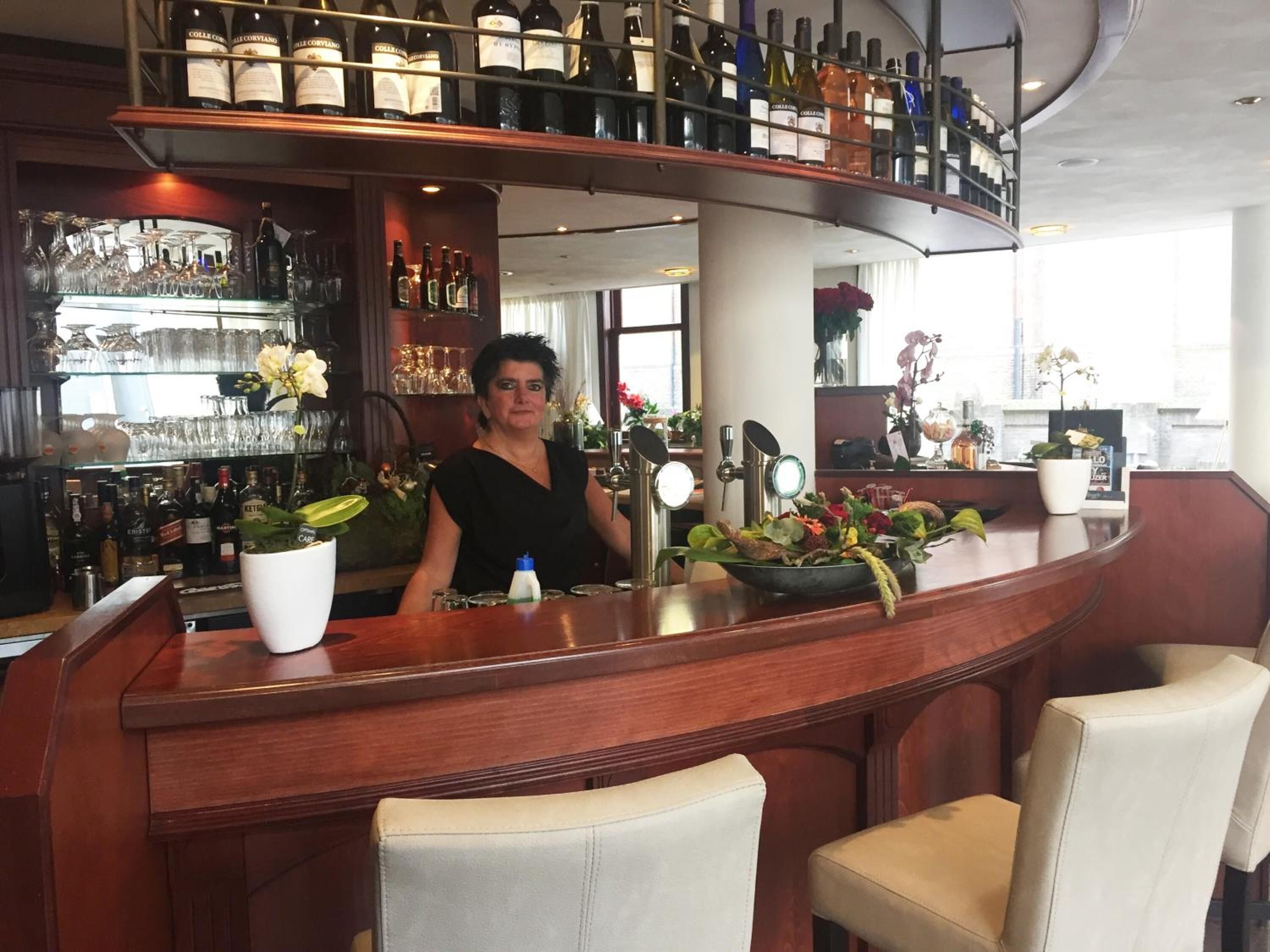 A bar area with a bartender, shelves of wine bottles, glasses, and a potted plant.