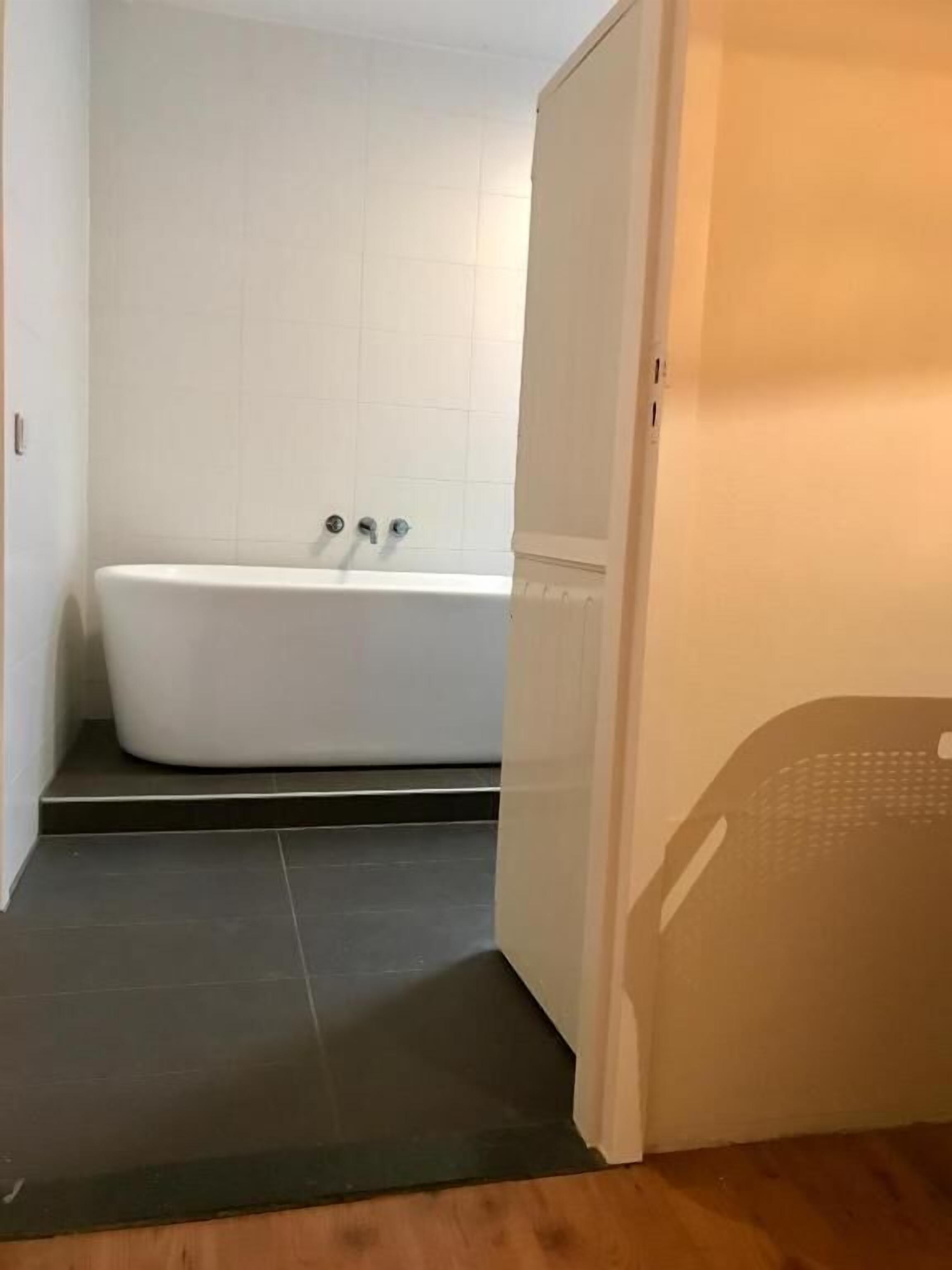 Ein Badezimmer mit einer weißen Badewanne, dunklen Bodenfliesen und Holzdielen.