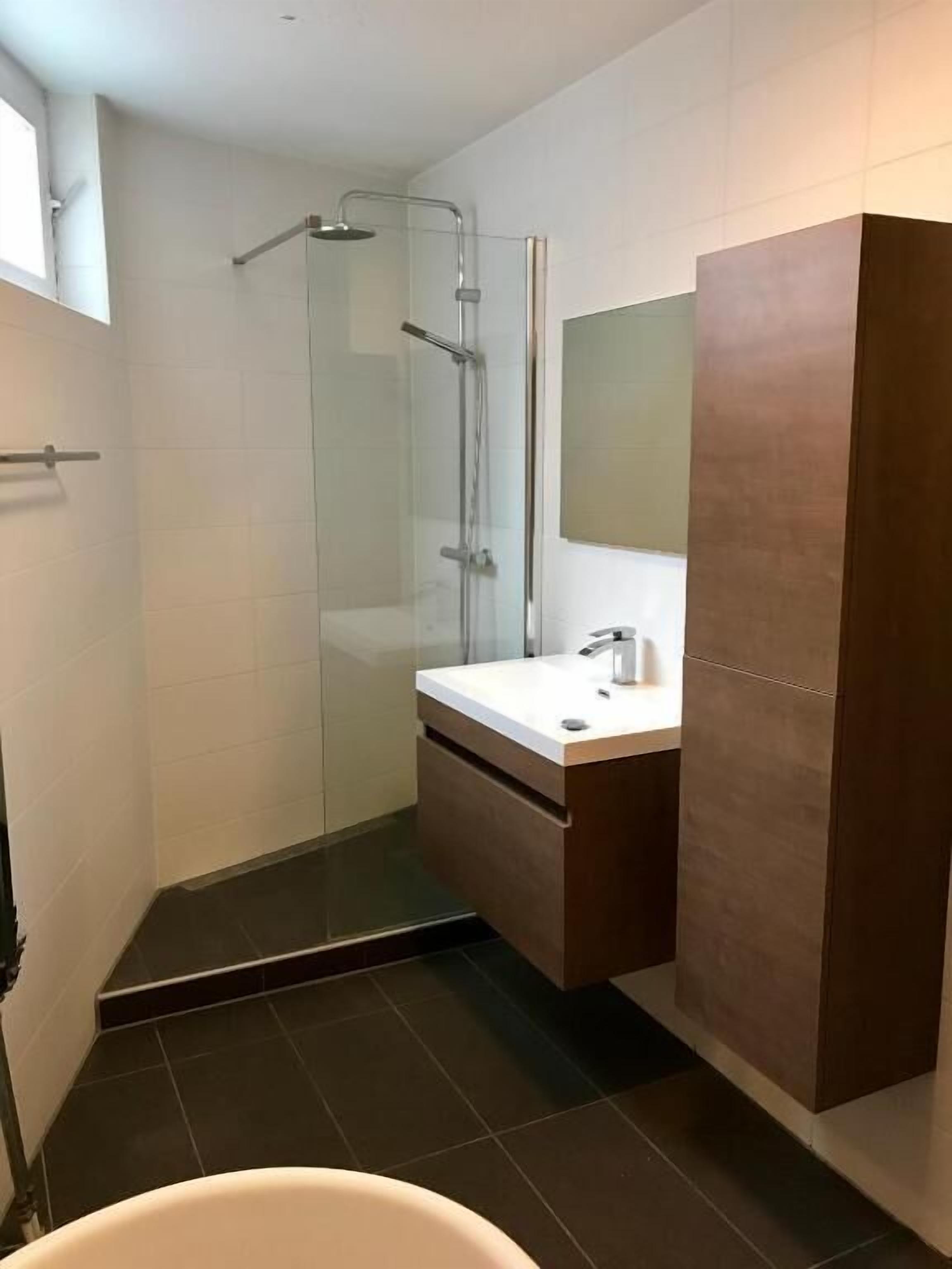 A modern bathroom with a glass shower enclosure, a white sink, and a large mirror.
