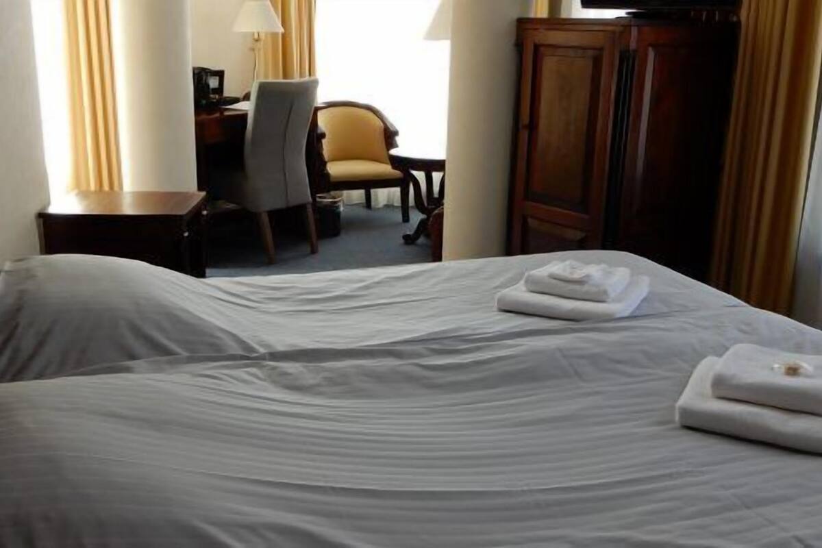 A hotel room with two beds, a desk, a chair, and a wardrobe.