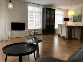 Una sala de estar con un televisor de pantalla plana, un comedor con mesa y sillas, y un mueble negro.