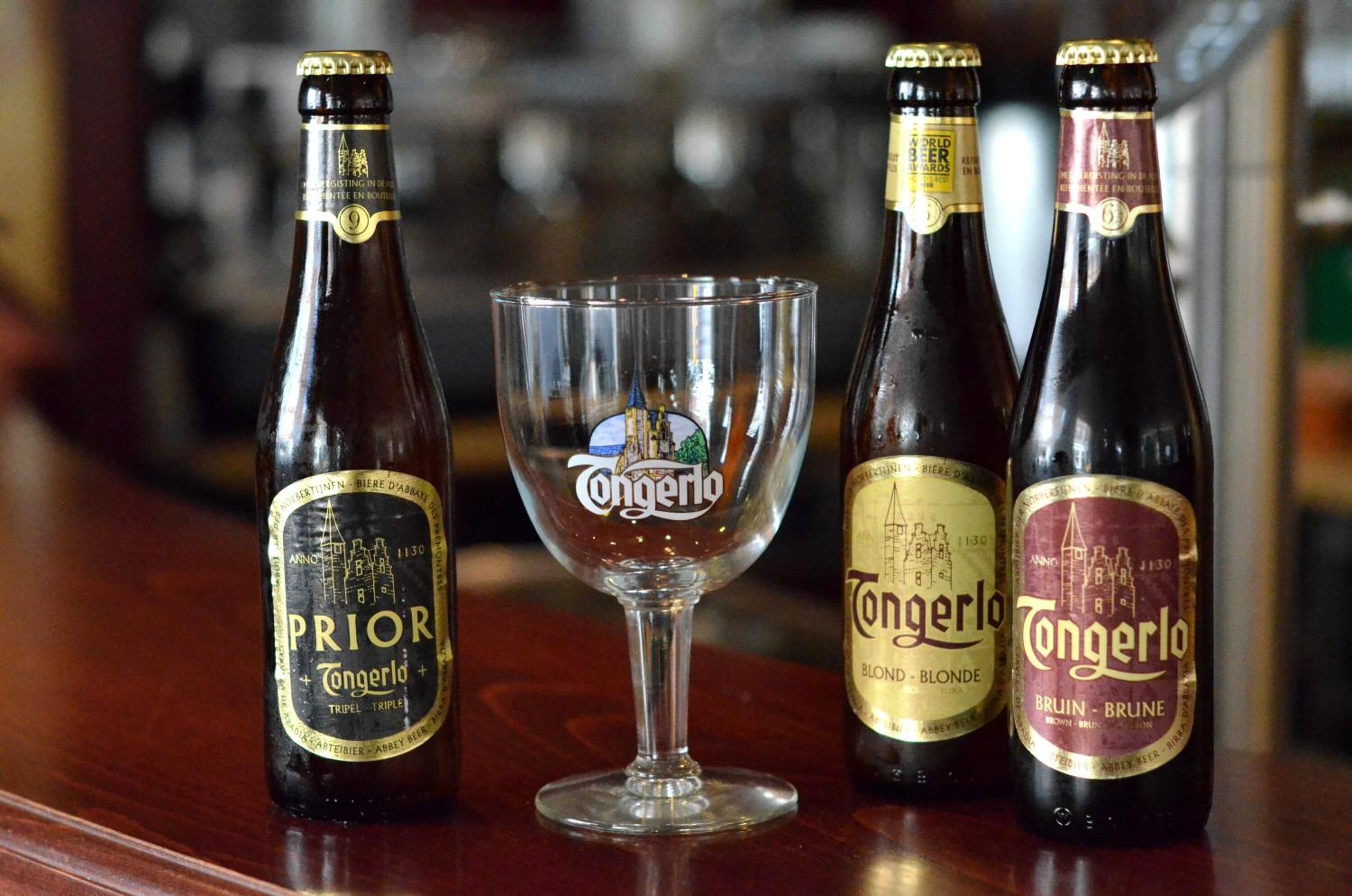 Three bottles of beer and a glass on a bar counter.