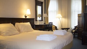 Een hotelkamer met een groot bed, twee nachtkastjes, een bureau, een stoel en een spiegel.