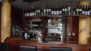 Een bar met een wijn- en drankendisplay, planken met glazen en een marmeren zuil.