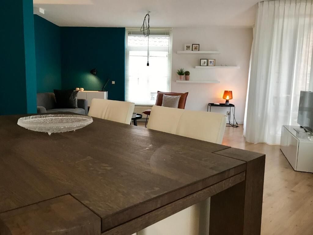 Ein Essbereich mit Holztisch und Stühlen, einem Fenster mit Jalousien, einer Lampe und einem Fernseher auf einem Schrank.
