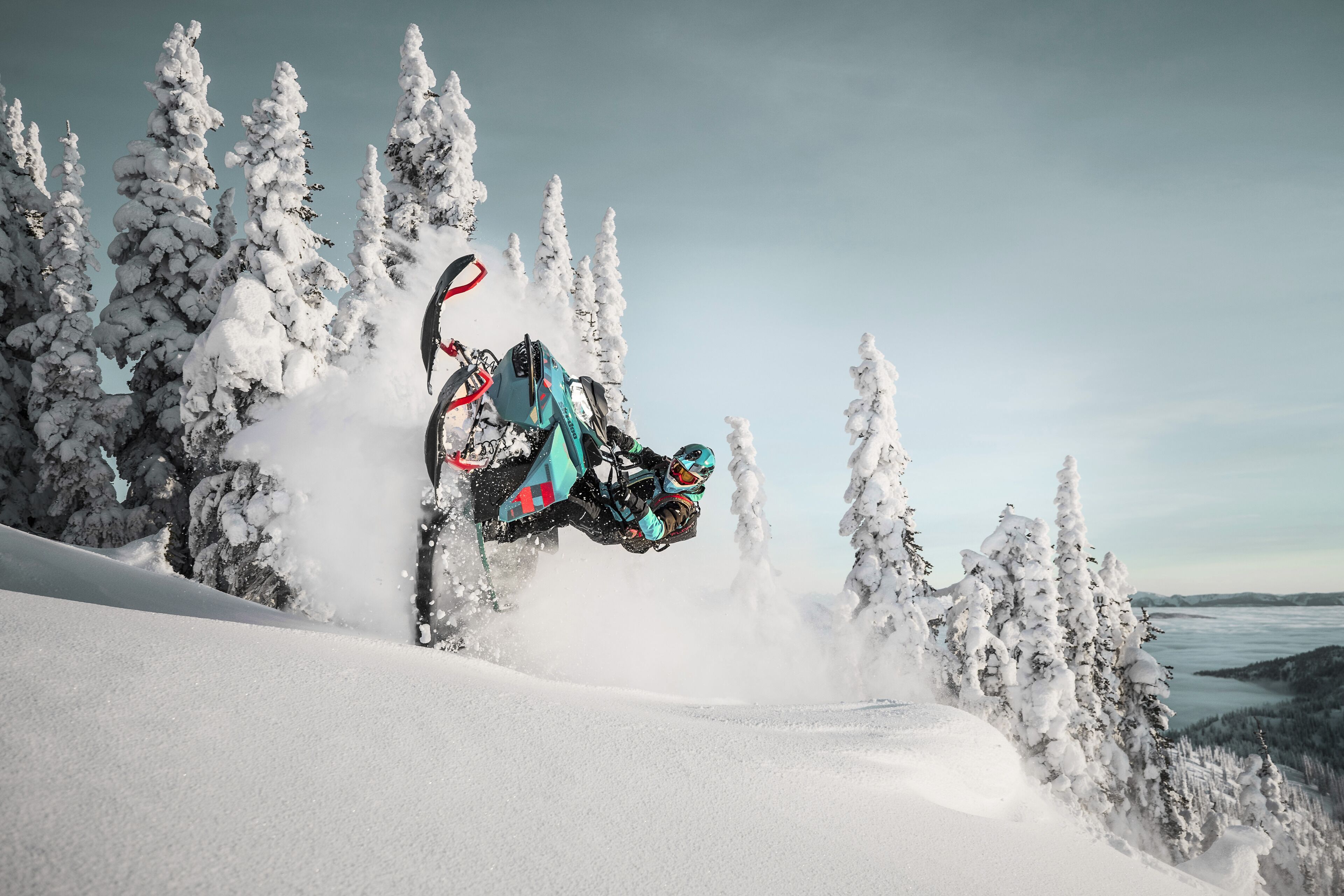 Una moto de nieve realizando un salto sobre un paisaje nevado con árboles.