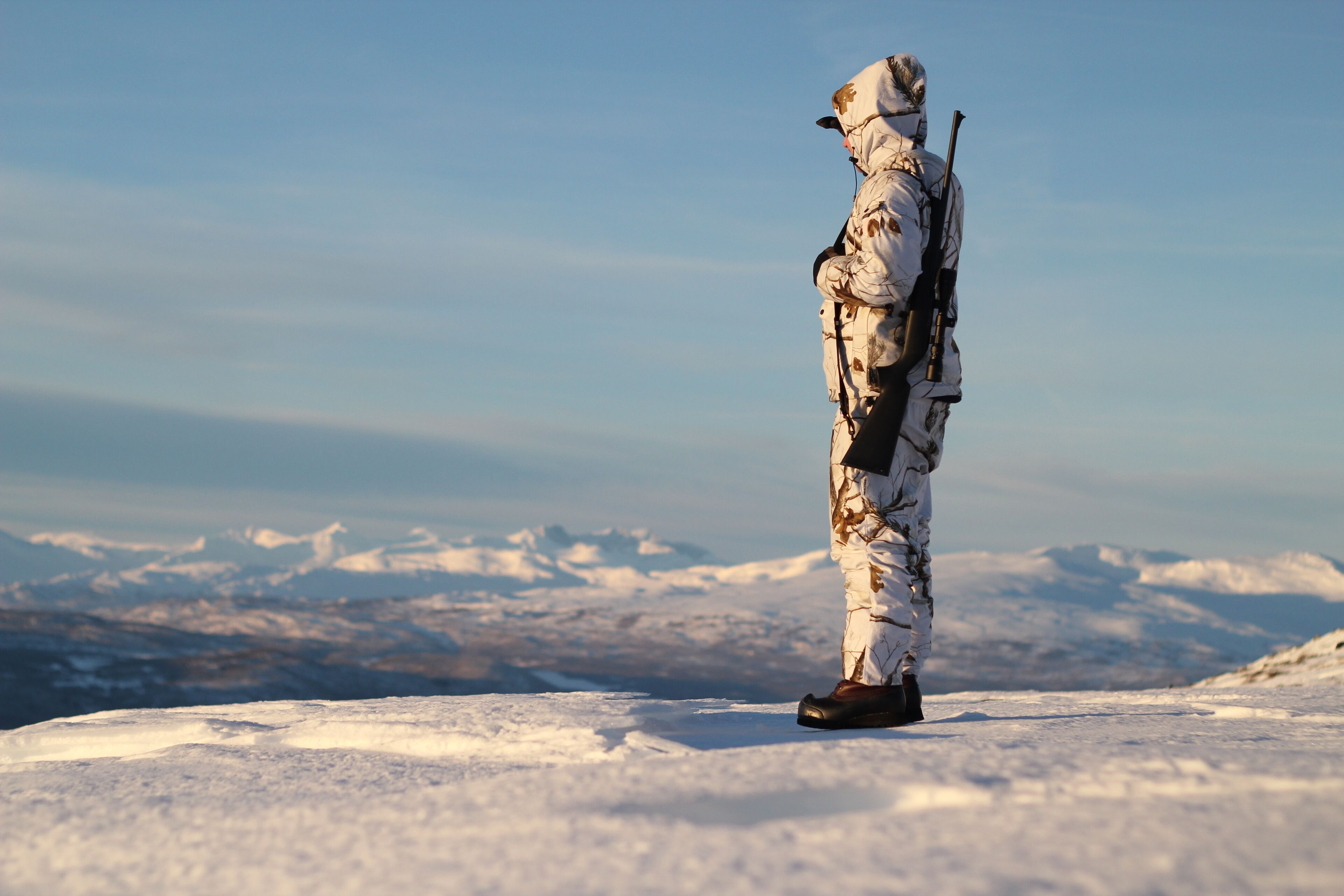 Une personne, vêtue pour l’hiver, se tient sur une surface enneigée, avec une chaîne de montagnes en arrière-plan.