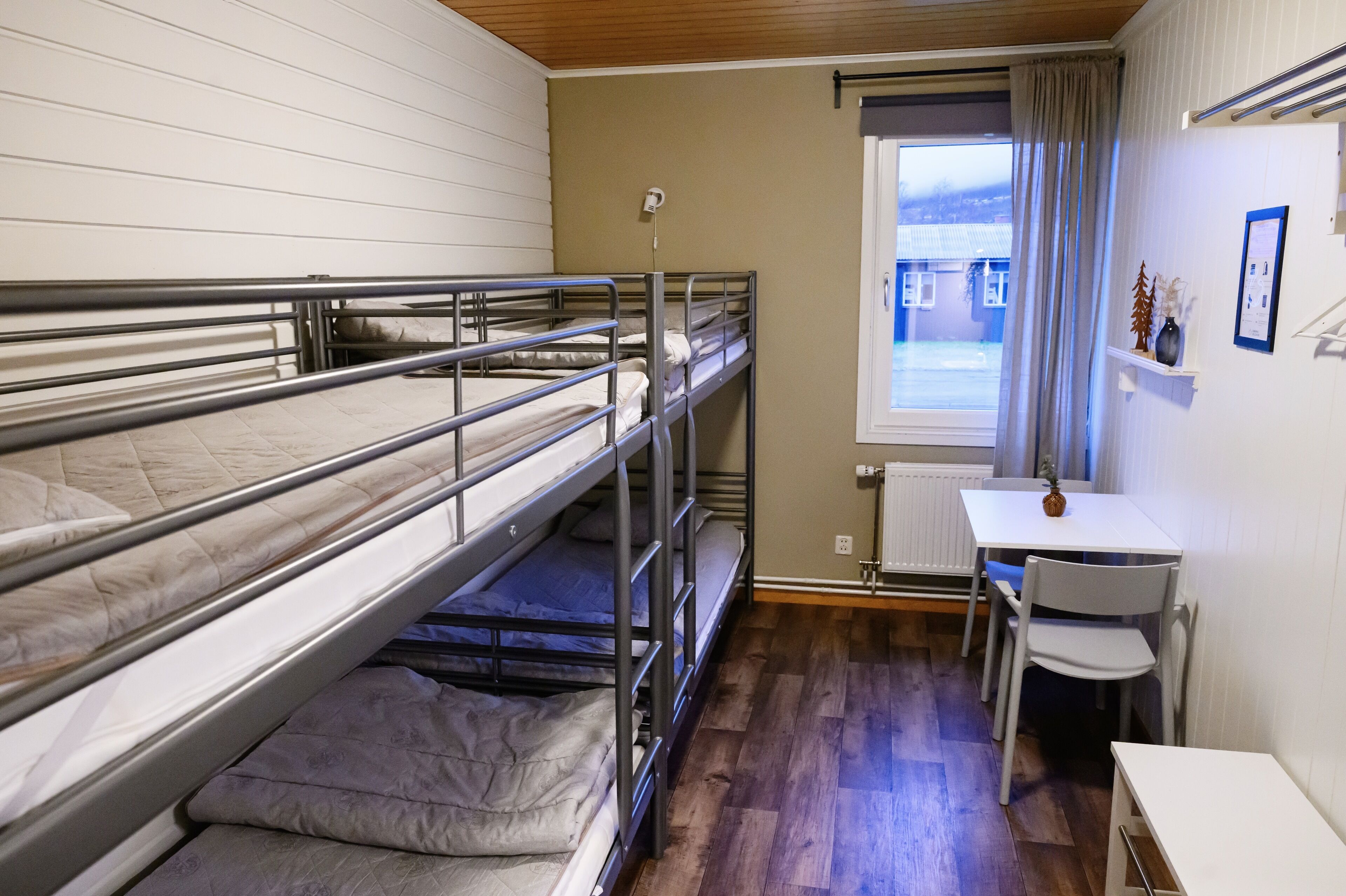 Ein Schlafzimmer mit Etagenbetten, einem kleinen Schreibtisch und Stuhl, einem Fenster mit Vorhängen und einem Heizkörper.