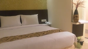 A hotel room with a bed, a nightstand, a vase, and a green suitcase. - Harmoni Inn Pelabuhan Makassar (Makassar)