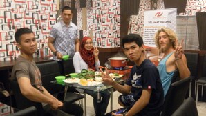 A group of people seated around a table with various dishes, in a room with patterned wallpaper and a sign indicating a hotel. - Harmoni Inn Pelabuhan Makassar (Makassar)