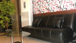 A black leather sofa with white stitching, a glass coffee table, and a patterned wall. - Harmoni Inn Pelabuhan Makassar (Makassar)