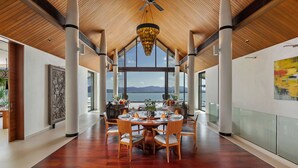 Un espace repas offrant une vue sur la mer, avec un plafond en bois et de grandes fenêtres.