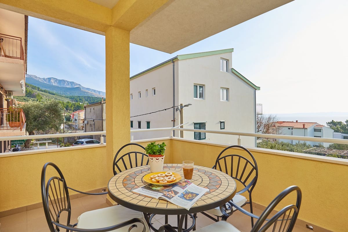 A balcony with a table, chairs, a potted plant, and a newspaper.