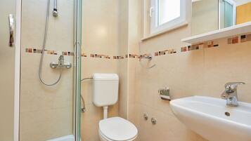 Une salle de bain moderne avec une douche à parois de verre, des toilettes blanches et un lavabo surmonté d’un miroir.