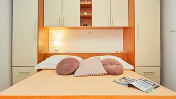A bedroom with a bed, pillows, a nightstand, and a shelf above the bed.