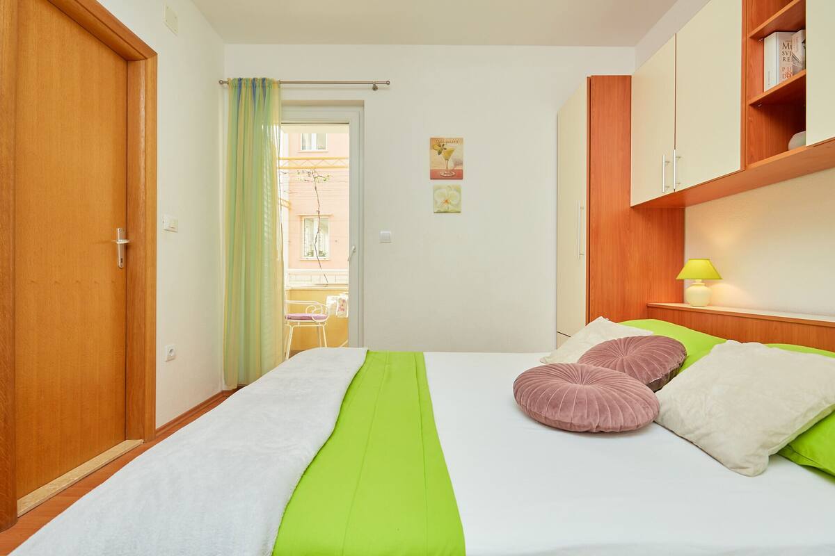 A bedroom with a bed, wooden wardrobe, and a small bedside table with a lamp.