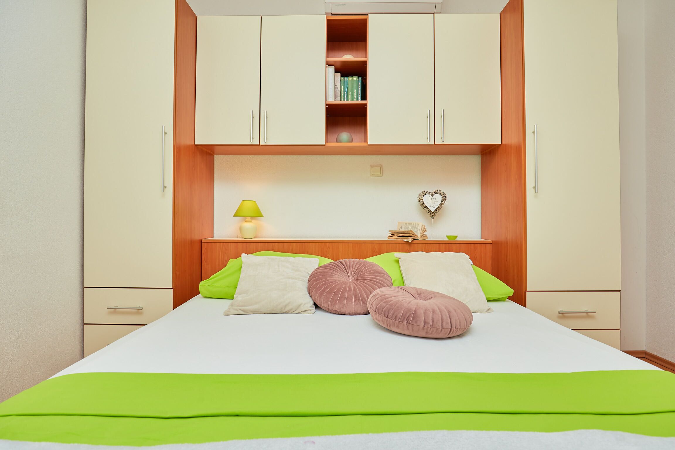 A neatly arranged bedroom with a bed, bedside tables, a lamp, and a heart-shaped decoration on the wall.