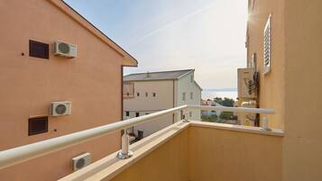 A balcony with a white railing, air conditioning units, and a view of neighboring buildings.
