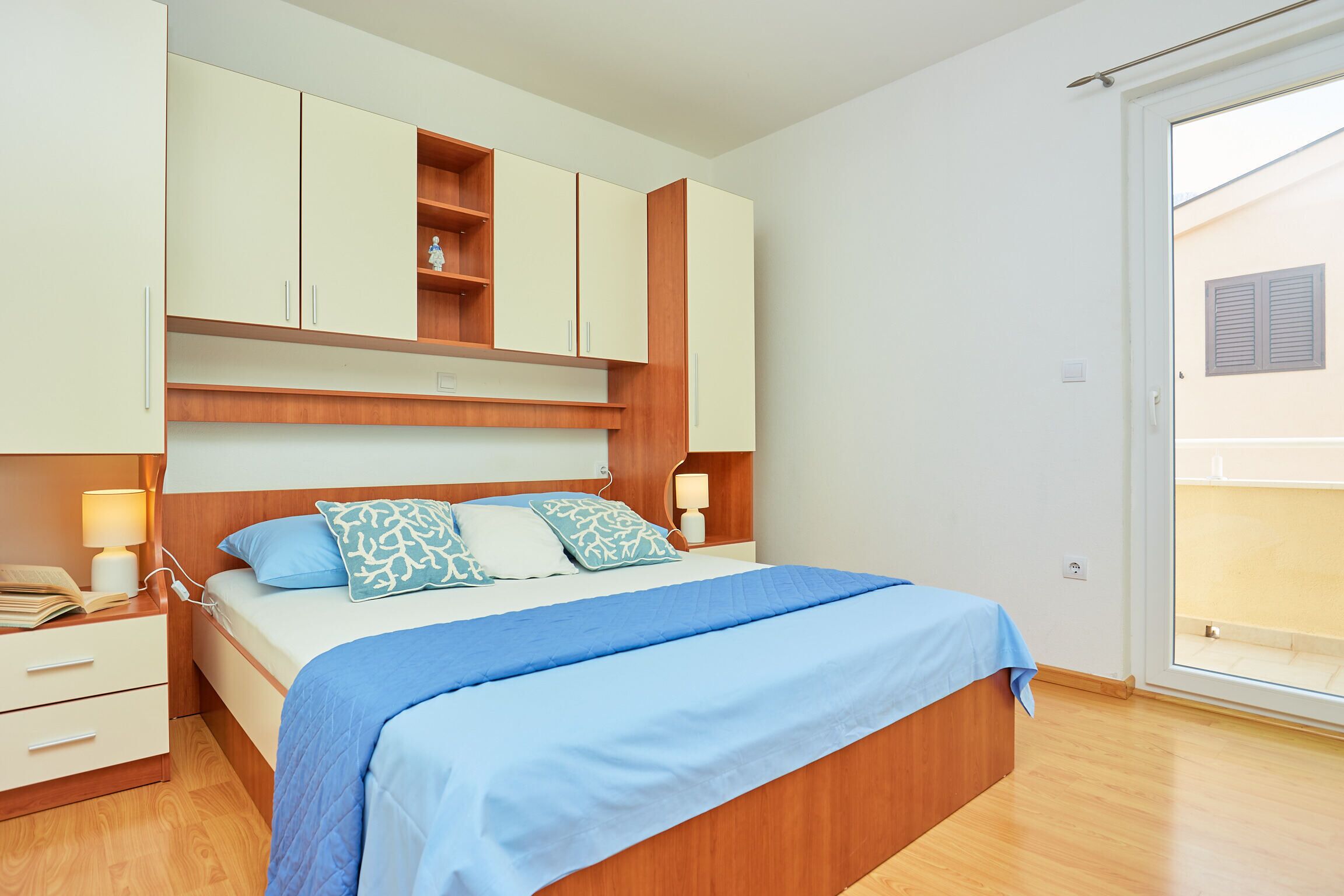A bedroom with a bed, bedside tables, a wardrobe, and a sliding glass door to an outdoor area.