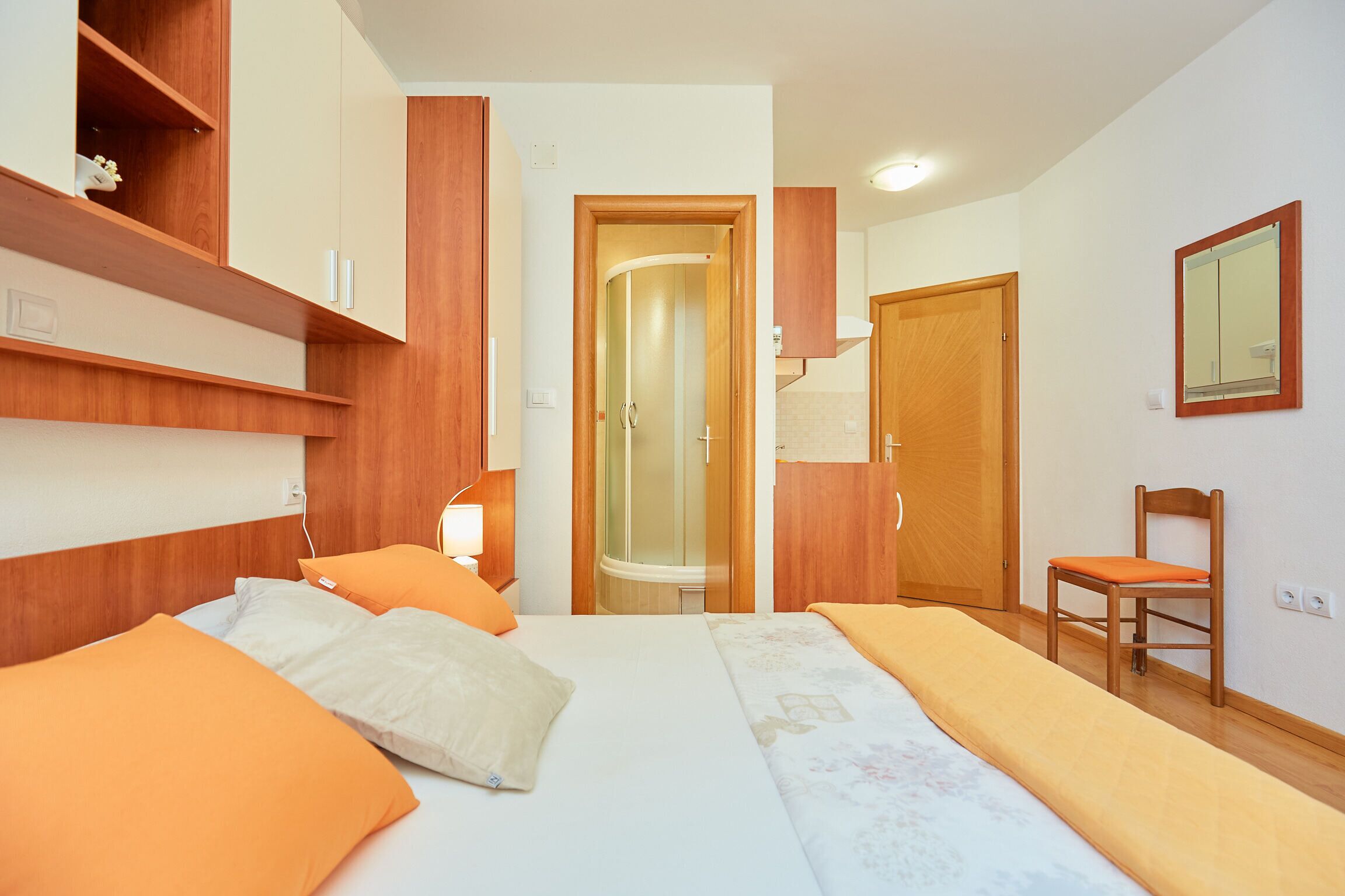 A hotel room with a bed, a chair, a shower, and wooden cabinetry.