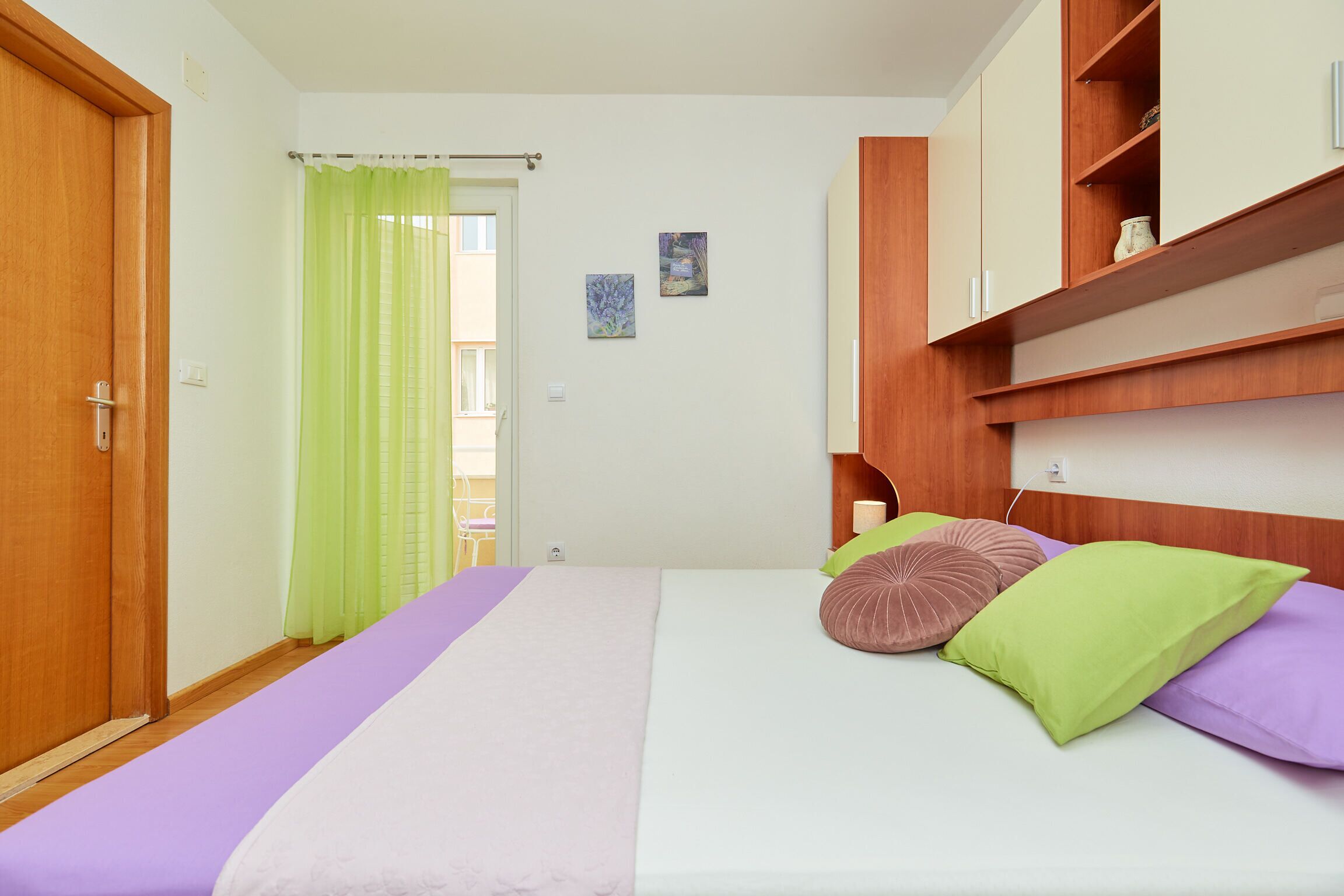 Une chambre à coucher avec un lit, une armoire en bois, un rideau vert et un petit tableau accroché au mur.