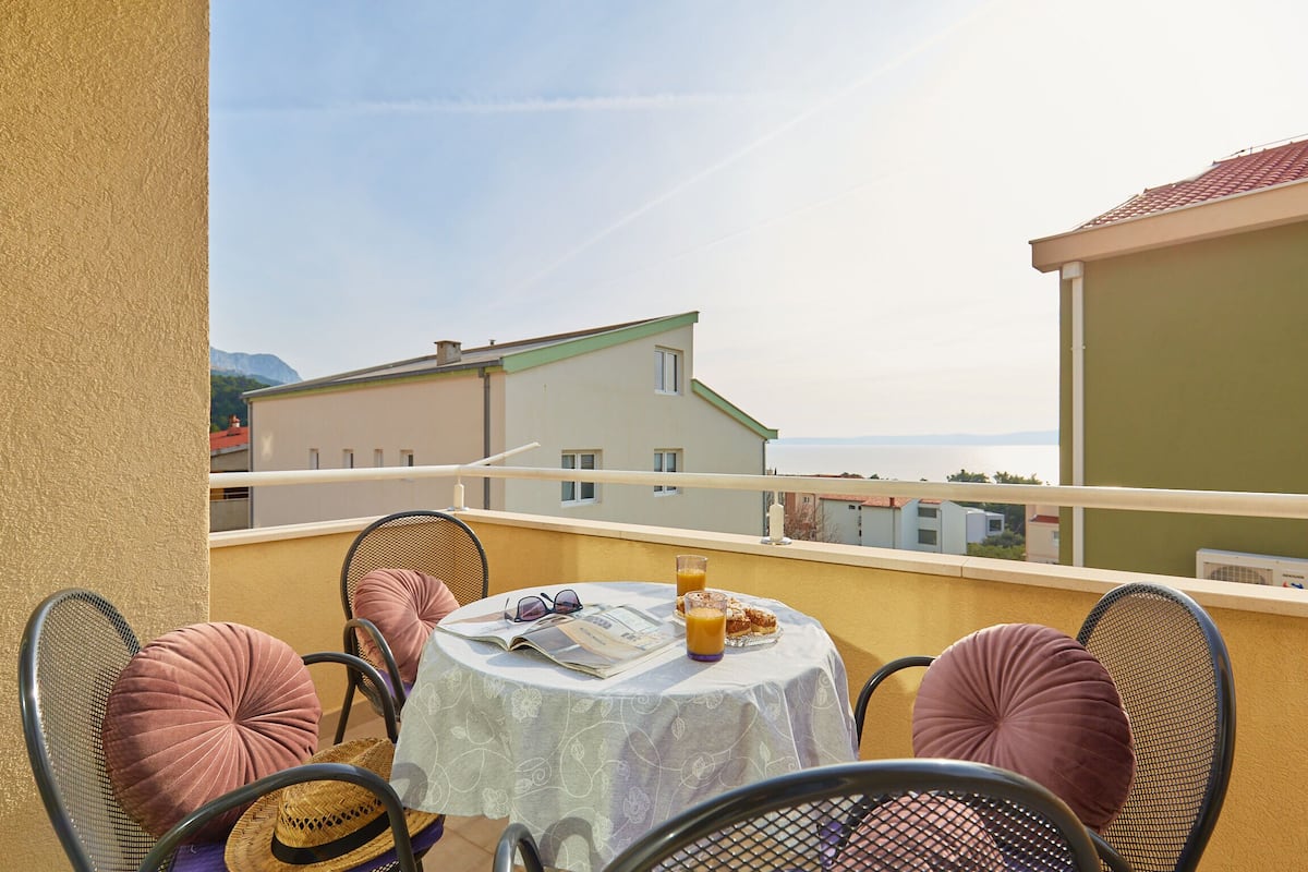 A balcony with a table set for two, featuring a newspaper, glasses, and a glass of orange juice.