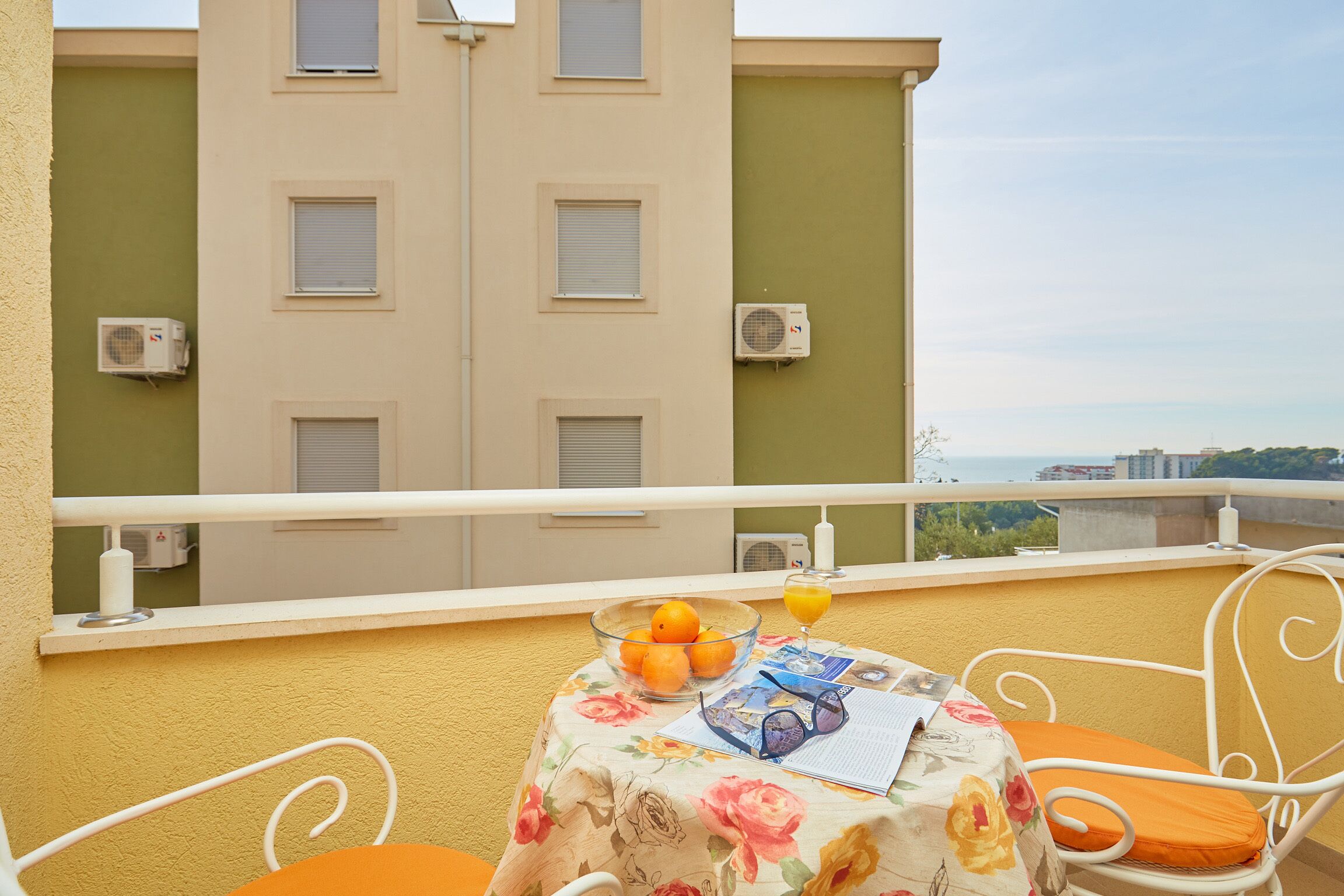 A balcony with a table set for two, featuring a bowl of oranges, a glass of orange juice, and a menu.
