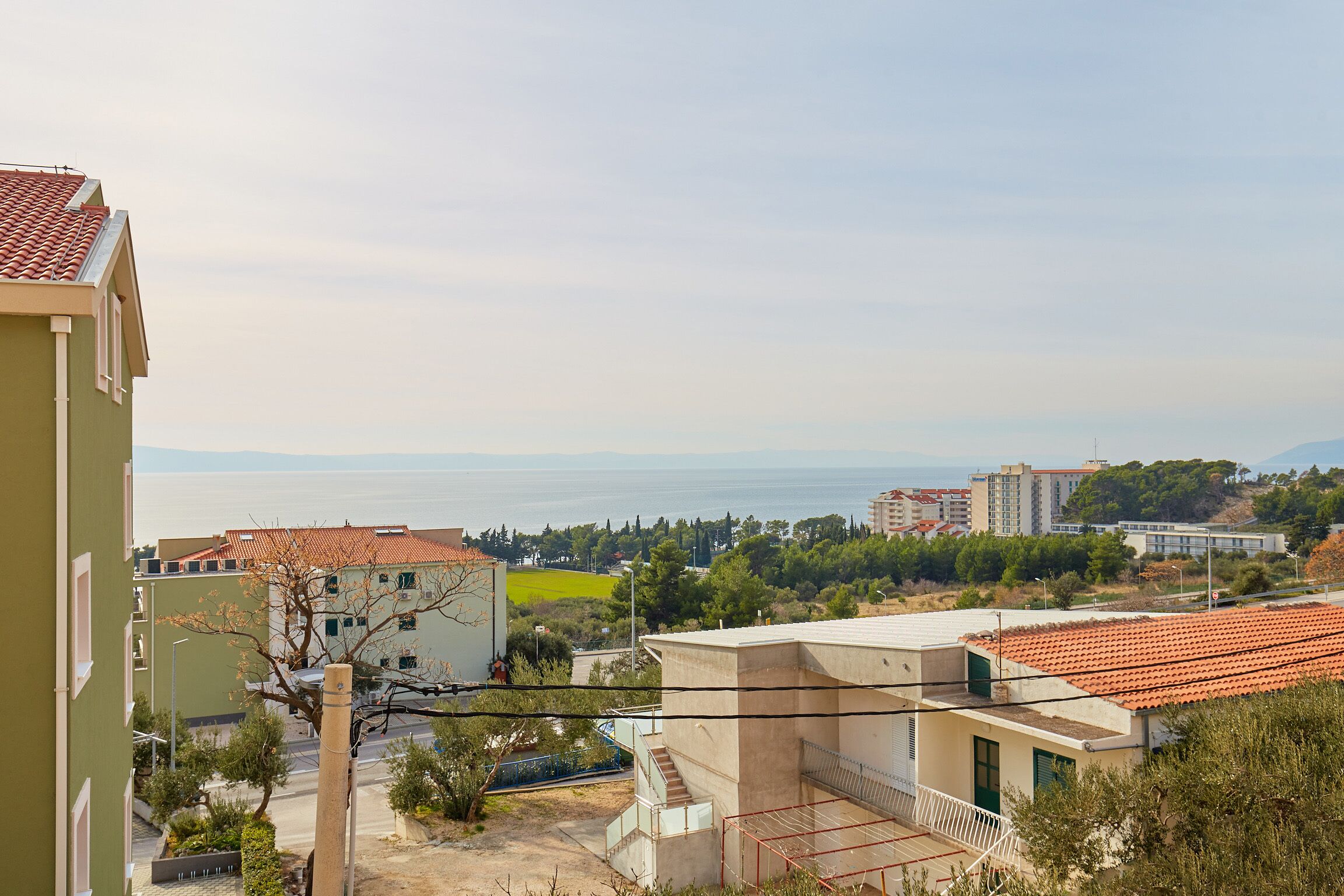 Un quartier résidentiel offrant une vue sur la mer, avec des bâtiments aux toits recouverts de tuiles rouges et un bâtiment vert en premier plan.