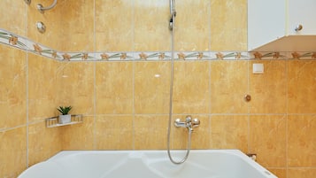 A bathroom with a white bathtub, a showerhead, and a small plant on a shelf.