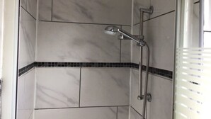 A shower with a handheld showerhead and a wall-mounted faucet, tiled with white and black tiles. - LPL Hôtel (Paris)