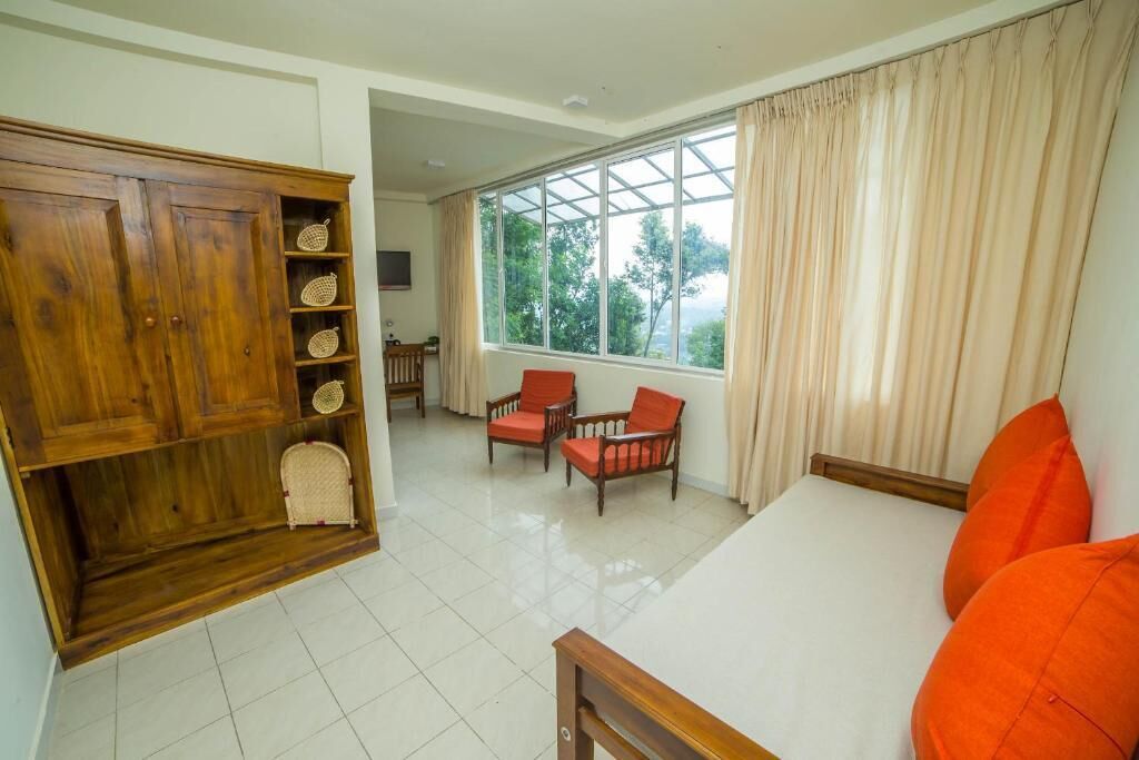 A room with a bed, a wooden wardrobe, two chairs, and a large window with curtains.