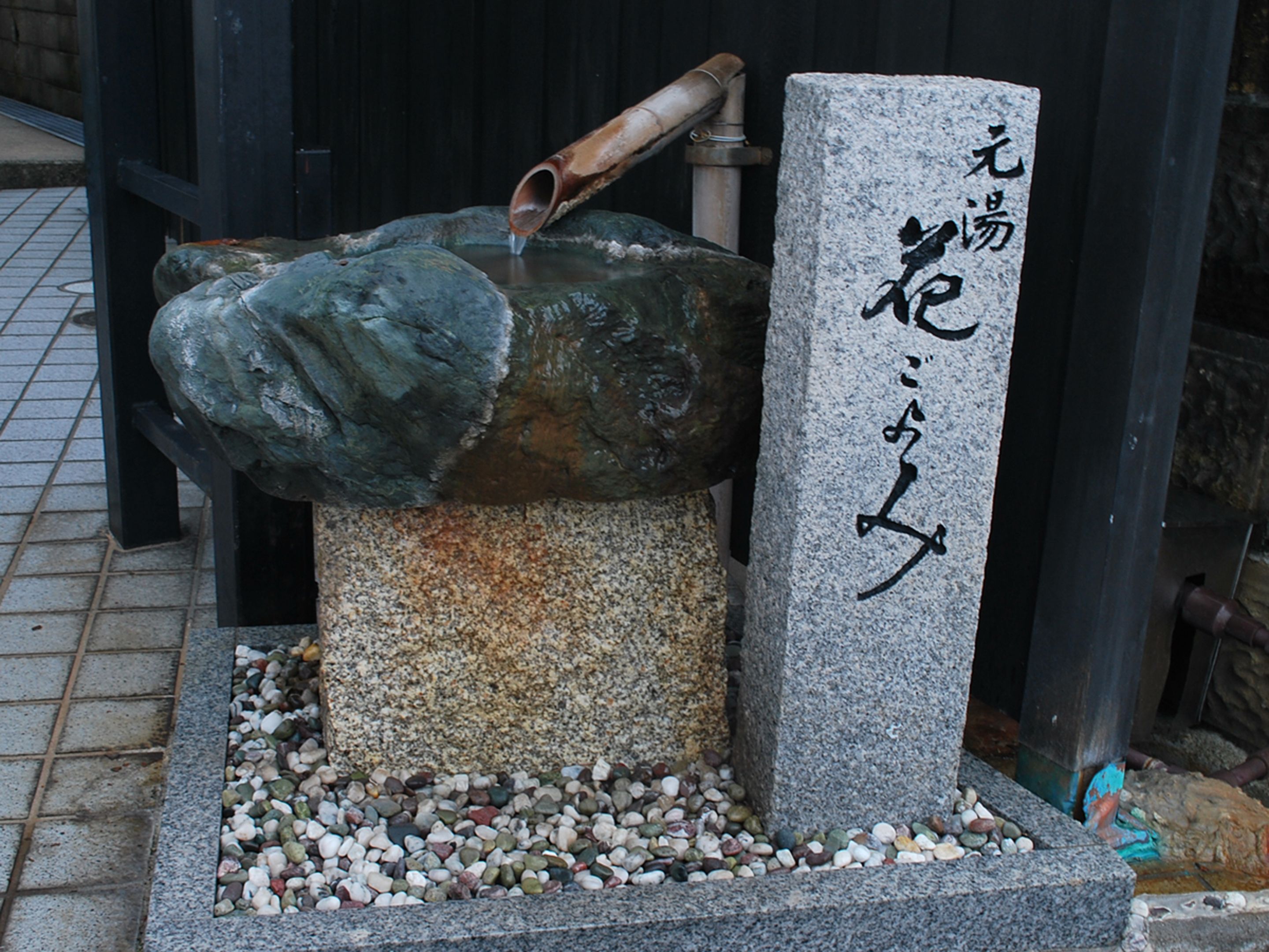 A stone fountain with a pipe and a stone with Japanese characters.